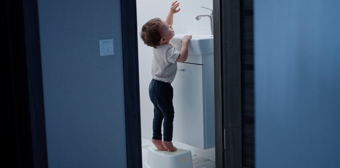 Child standing on a footstool to wash his hands at the basin